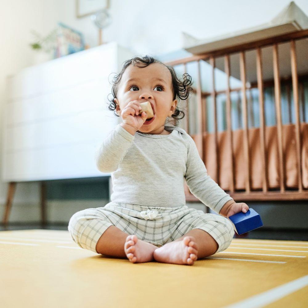 A baby sitting on the floor in it's bedroom at home while playing or looking curious.