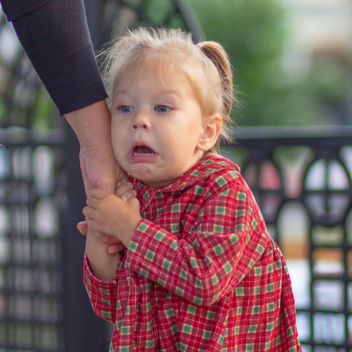 Caucasian little girl of 2 years with scared face holding hand of mother in summertime outdoors