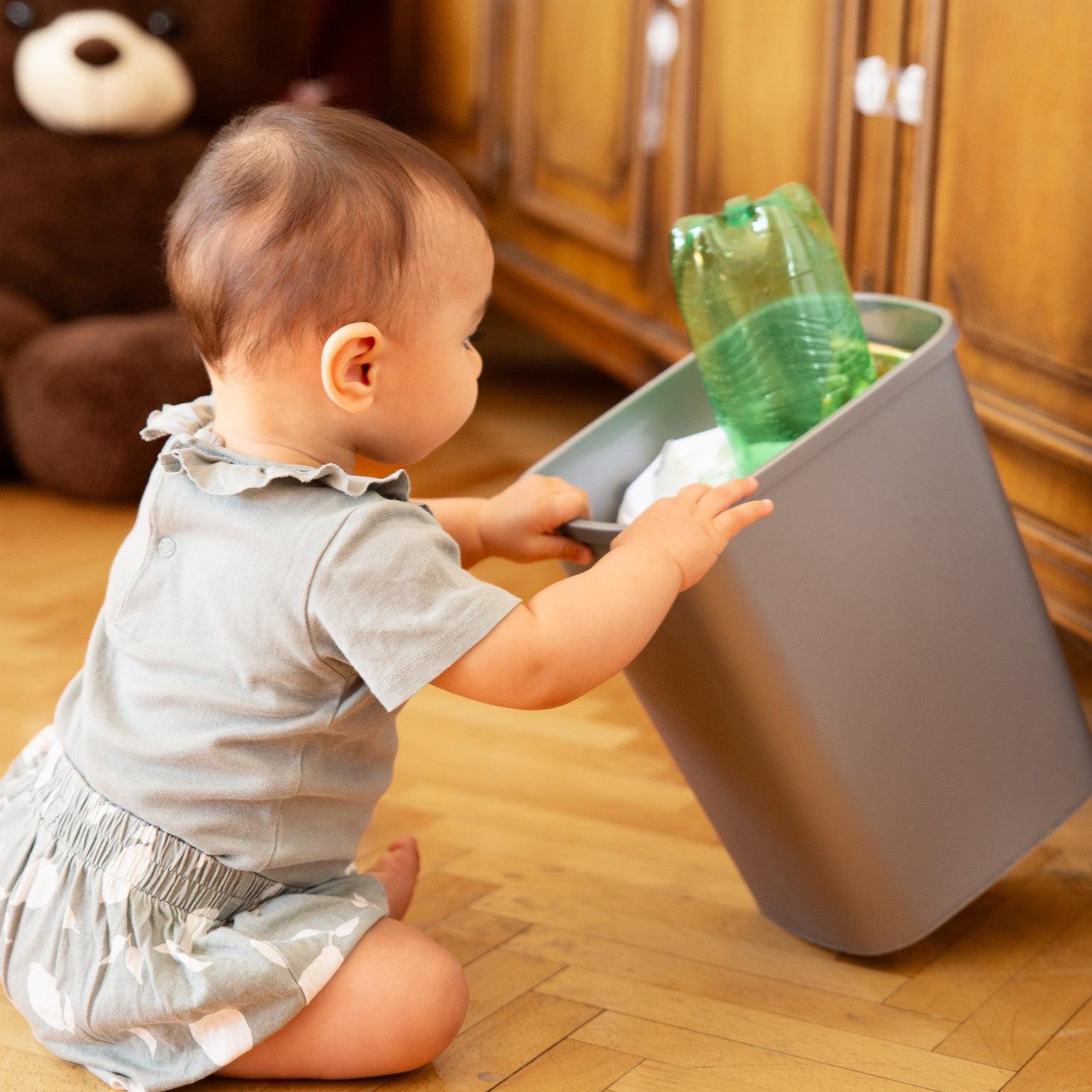 "The baby is peeking into the trash can.
