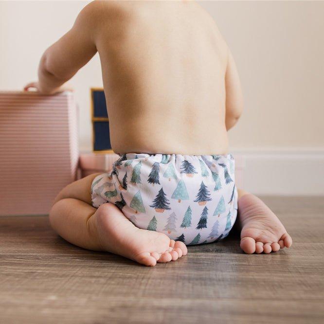 An 11-Month-Old Christmas Baby Boy with 12 Toes Wearing a Sustainable Christmas Cloth Diaper Sitting on a Wooden Floor Playing with Christmas Presents