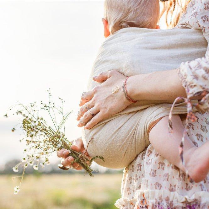 Mother is holding and tickling her baby, babywearing in sling