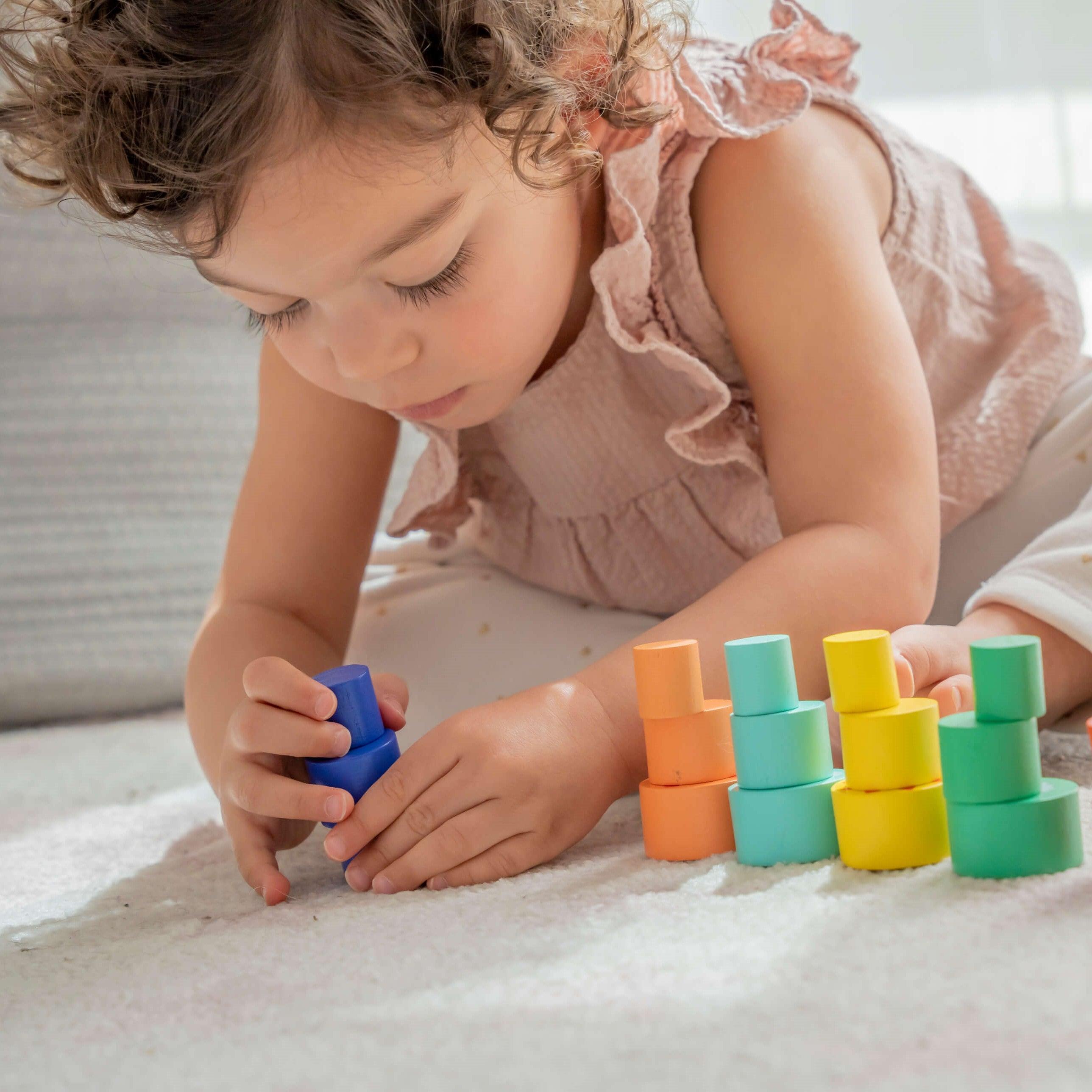 beautiful little girl has fun stacking blocks and pieces of sustainable wood of different colors