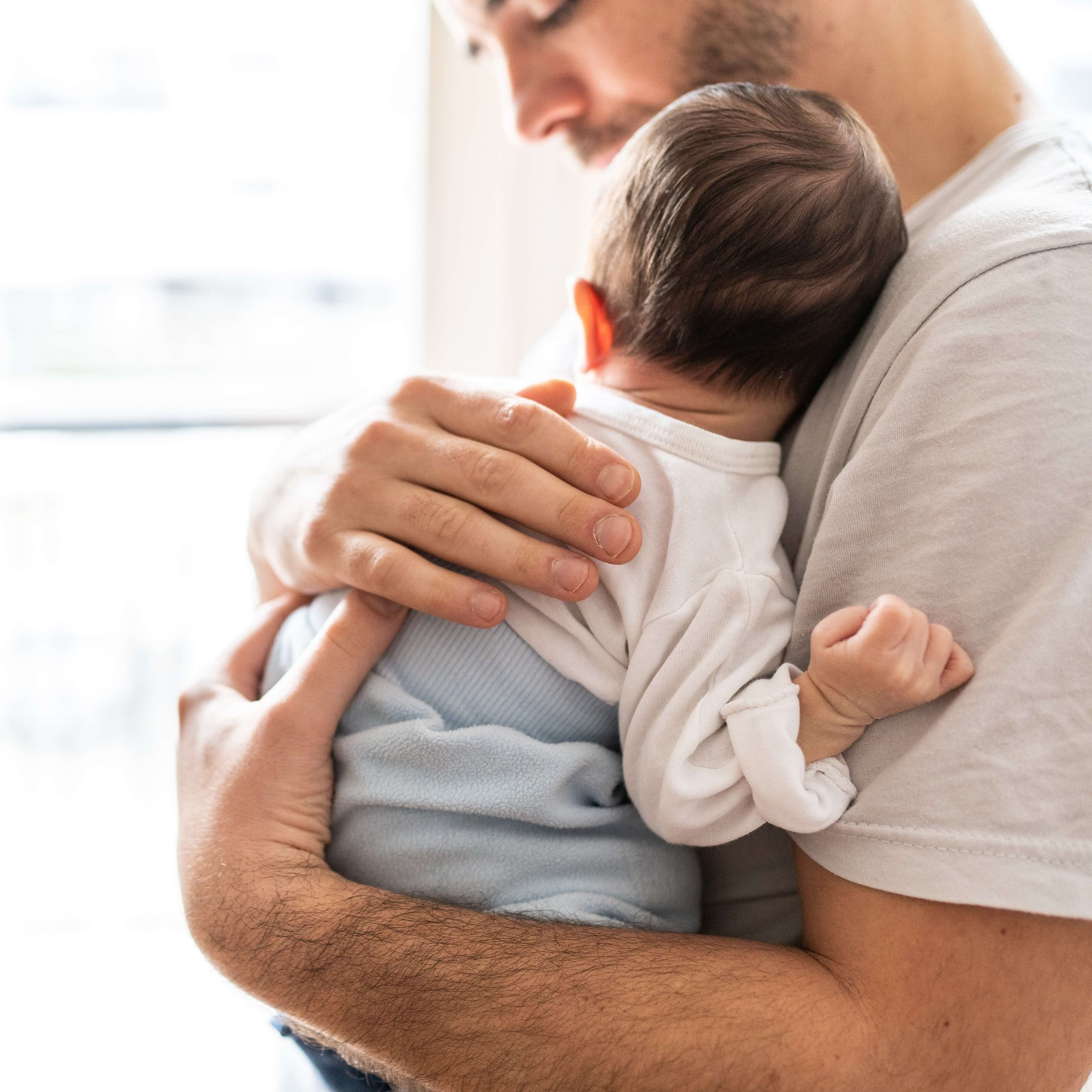 A new father is holding his newborn baby.