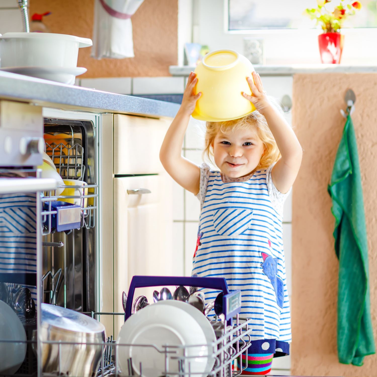 Little adorable cute toddler girl helping to unload dishwasher. 