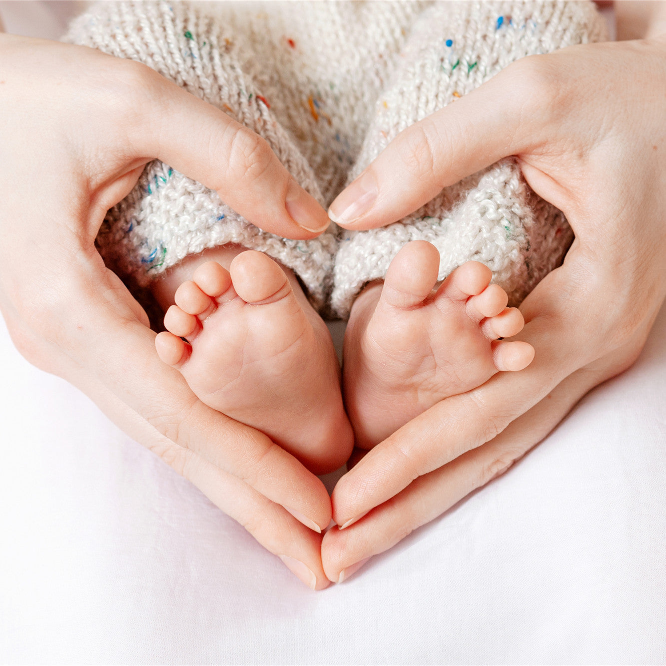 Tiny Newborn Baby's feet on female Heart Shaped hands closeup