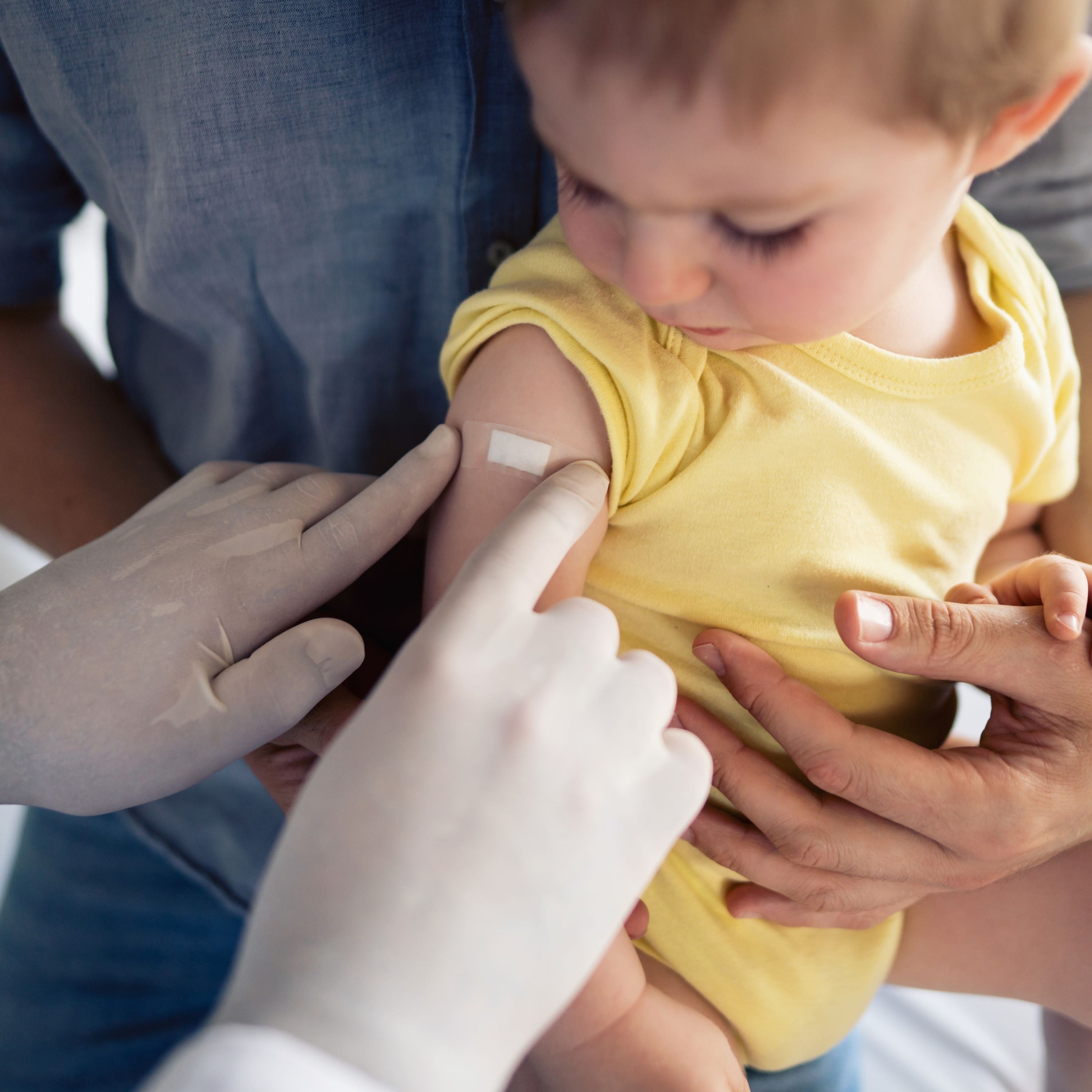 One unrecognizable doctor putting a patch on the little boy's shoulder after successful vaccination