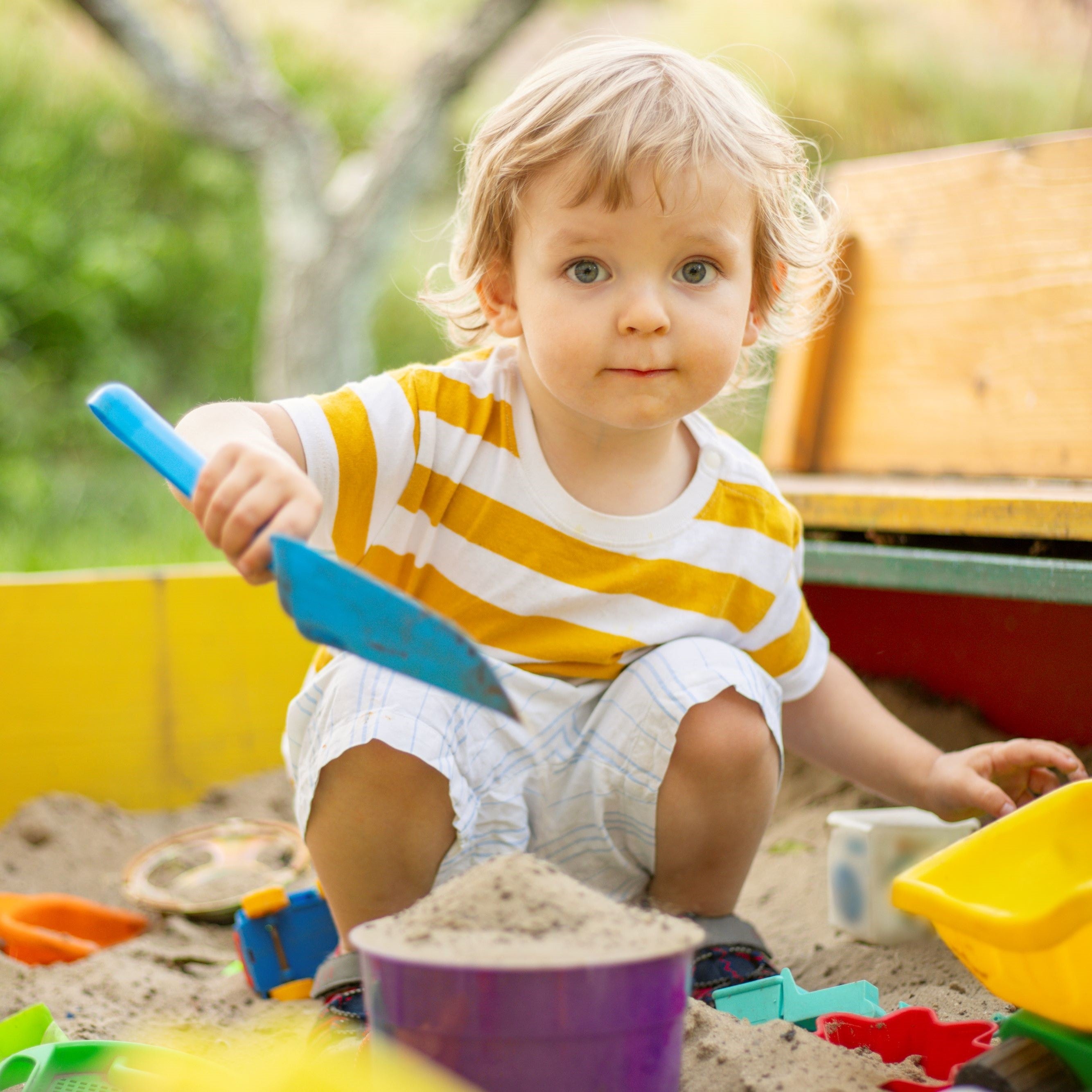 A little boy playing in the sandbox at the playground outdoors.