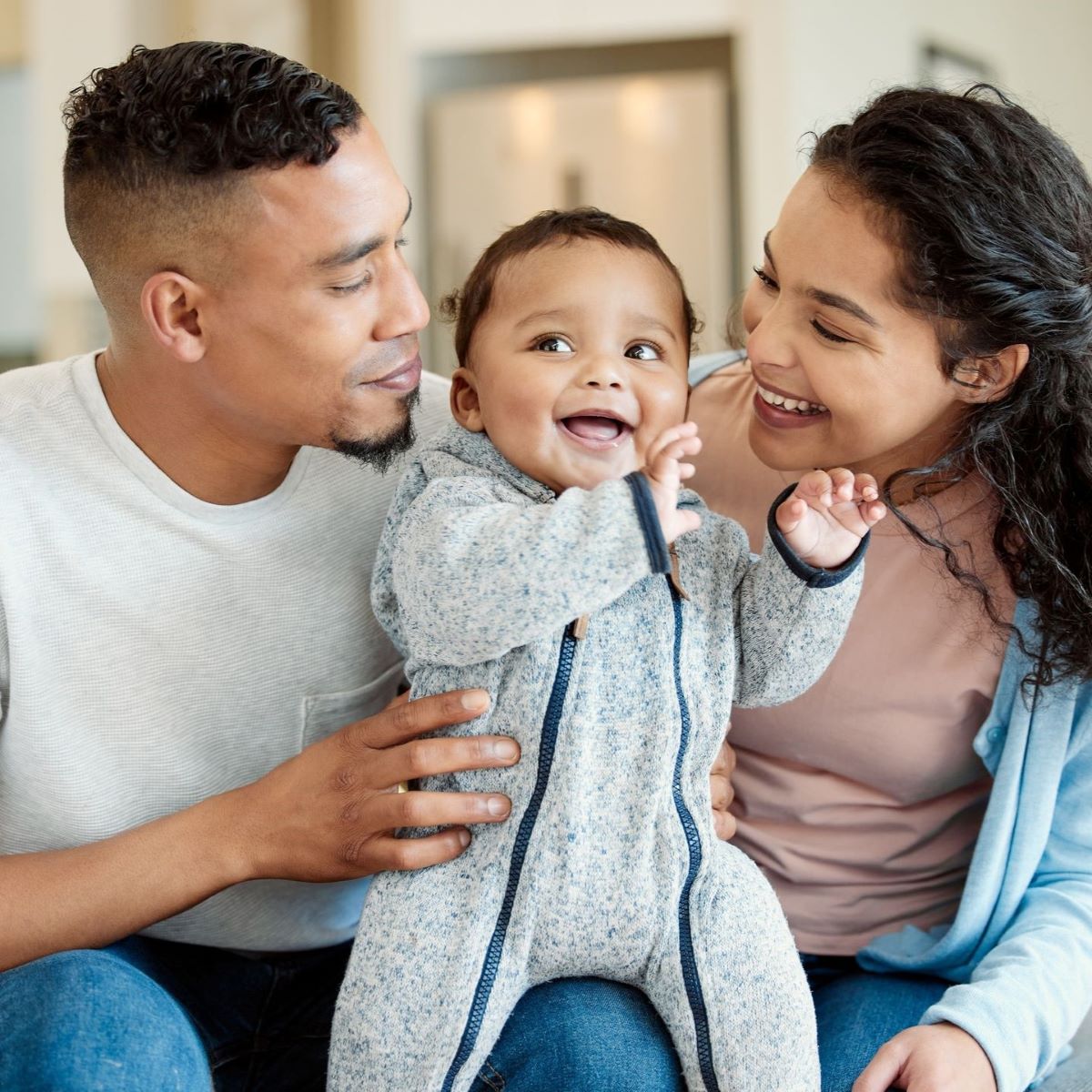 The mom and dad smile as they gaze lovingly at their baby.