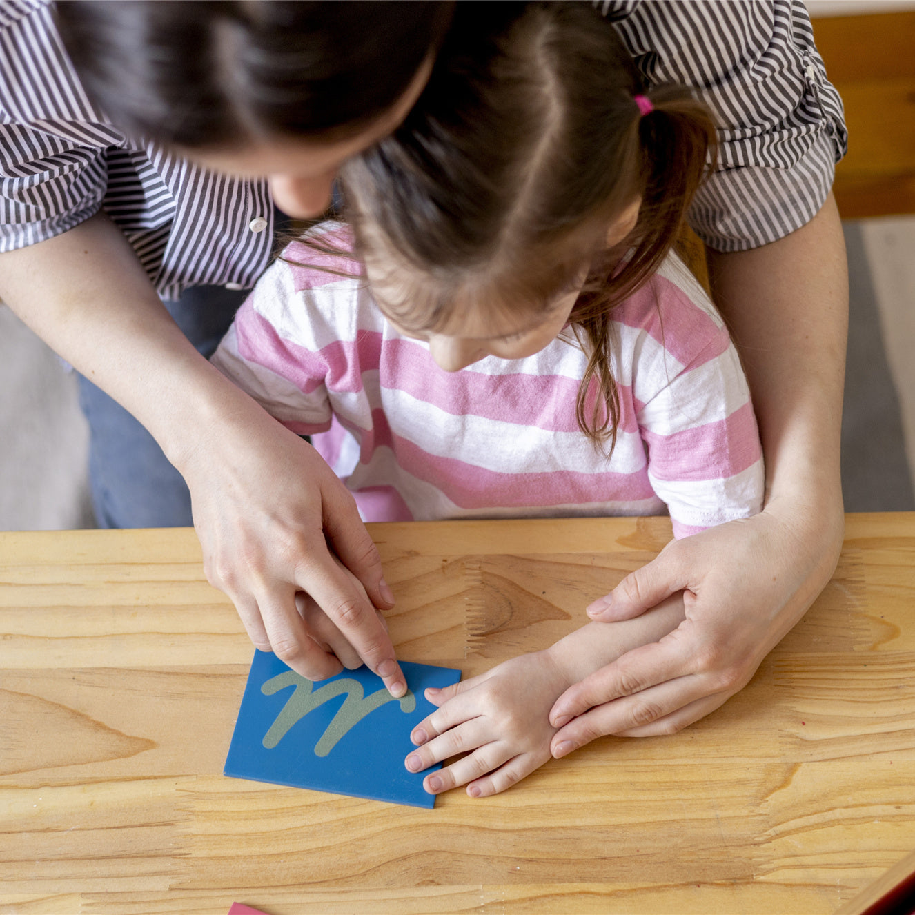 Montessori material. Mom helps her daughter learn letters using the rough alphabet.