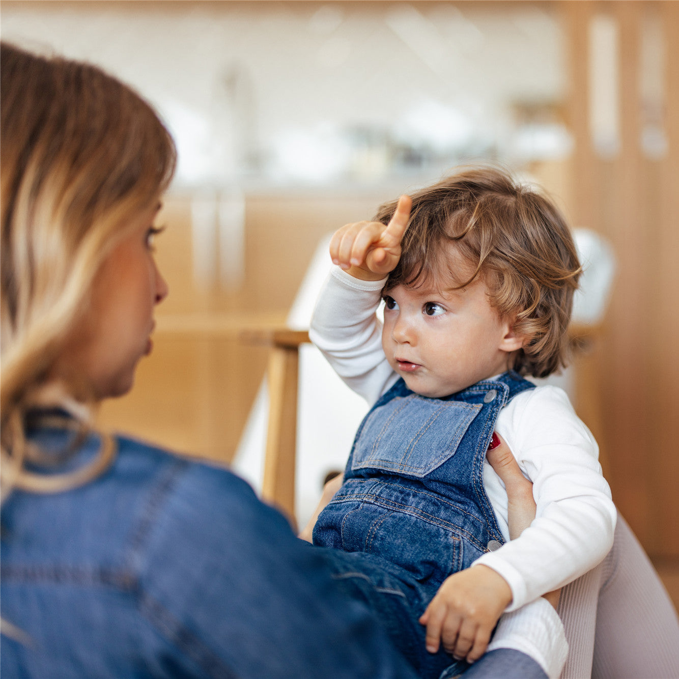 A toddler with curly blonde hair is talking with mom