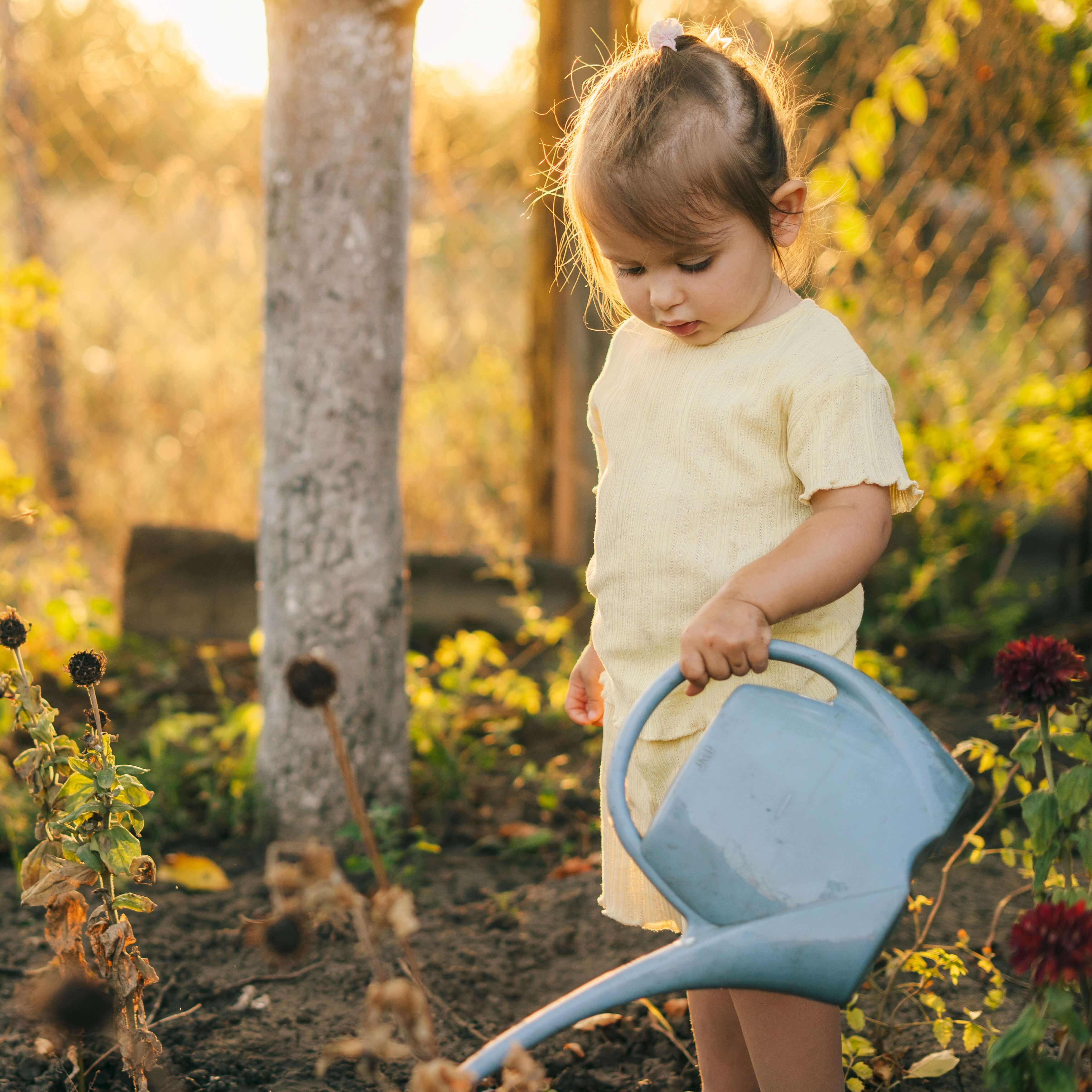 Girl in her flower garden, working in holiday watering plant flowers with watering can. 