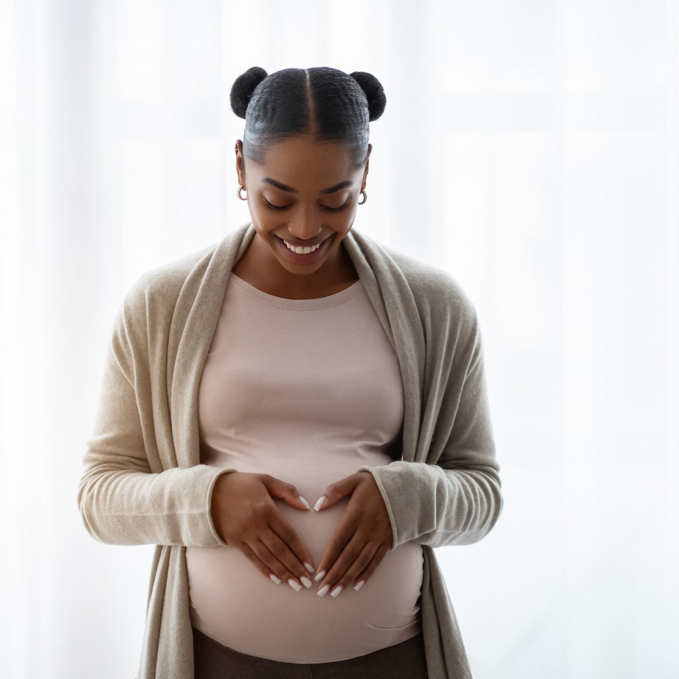 Smiling young black pregnant woman wearing comfy clothing holding hands on her big belly