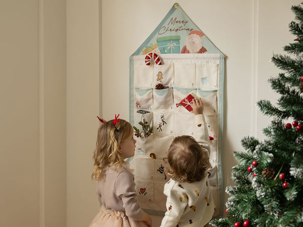 Two children looking at a Christmas-themed hanging organizer with a decorated tree in the background.