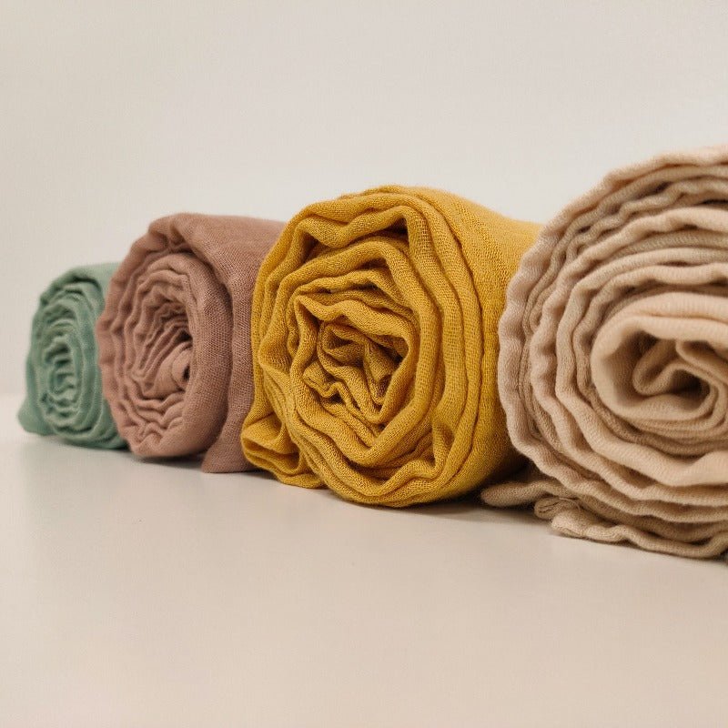 Four rolled-up cloths in green, pink, yellow, and beige on a light background